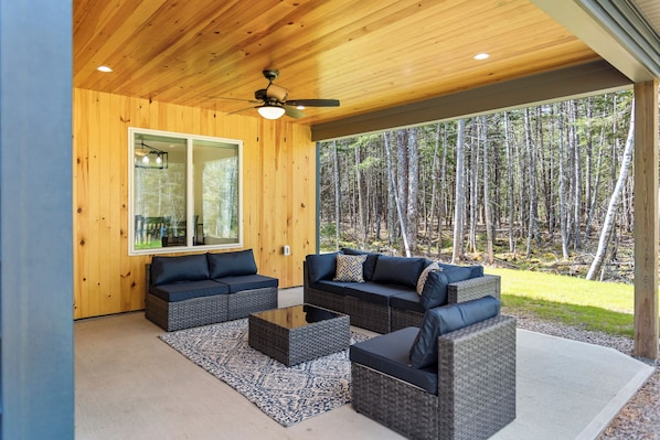 A covered outdoor seating area with wicker furniture and a ceiling fan. - The Retreat at Seal Point-New! (Lamoine)