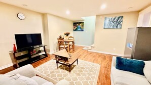 A living room with a TV, sofa, coffee table, and dining area. - Elegant 1BR Retreat Near Downtown Relax in Comfort (Dieppe)