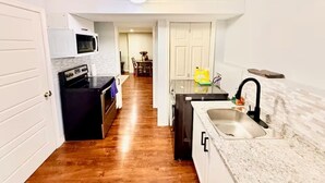 A compact kitchen with a microwave, oven, and sink, leading to a dining area with a table and chairs. - Elegant 1BR Retreat Near Downtown Relax in Comfort (Dieppe)