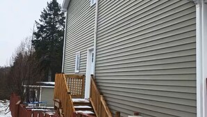 A building exterior with a wooden staircase, a metal fence, and an air conditioning unit. - Elegant 1BR Retreat Near Downtown Relax in Comfort (Dieppe)