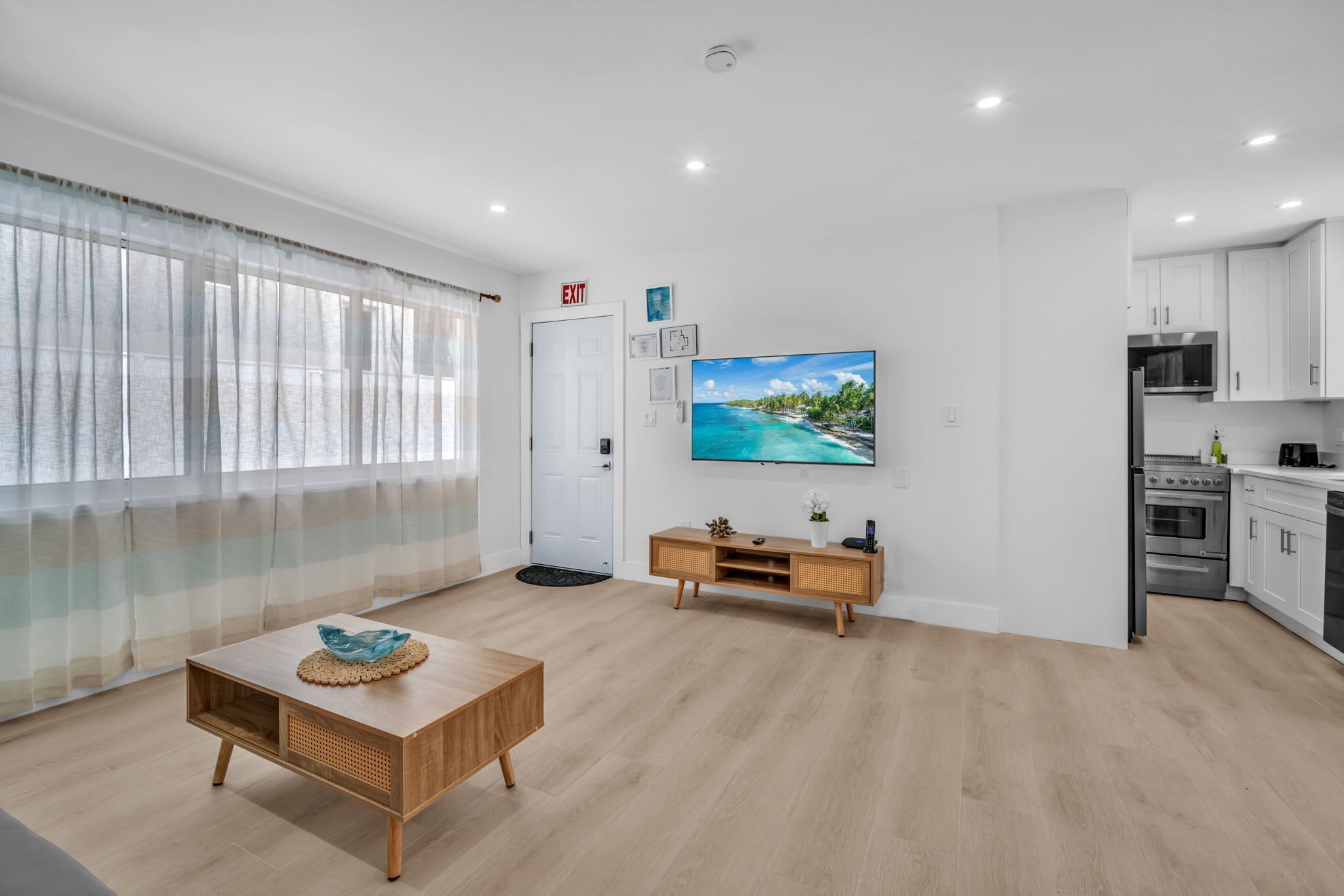 A modern living room with a wooden coffee table, a television, and a kitchen area with cabinets and appliances.