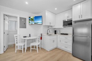 A modern kitchen with white cabinets, a stainless steel refrigerator, a coffee maker, and a small dining table with chairs. - #2 - Beachside Studio  Steps to Hollywood Beach (Hollywood)
