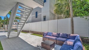 Eine moderne Außenveranda mit einem Korbsessel, einem Glastisch und einer Metalltreppe.