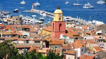 Une ville côtière qui se distingue par une tour jaune et rouge imposante, de nombreux bateaux dans le port et des bâtiments traditionnels aux toits de tuiles rouges.