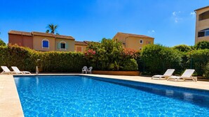 En klar, blå swimmingpool med liggestole og en hæk i baggrunden.