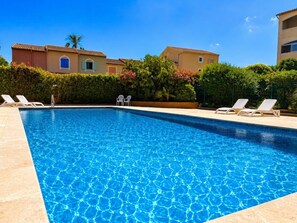 A clear blue swimming pool with lounge chairs and a hedge in the background.