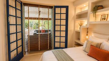 Une chambre à coucher avec un lit, une fenêtre avec des stores, une étagère avec des objets décoratifs et une vue sur l’extérieur.