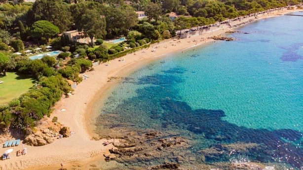 Oversigtsbillede af et kystområde med strand, klart blåt vand og frodig vegetation.