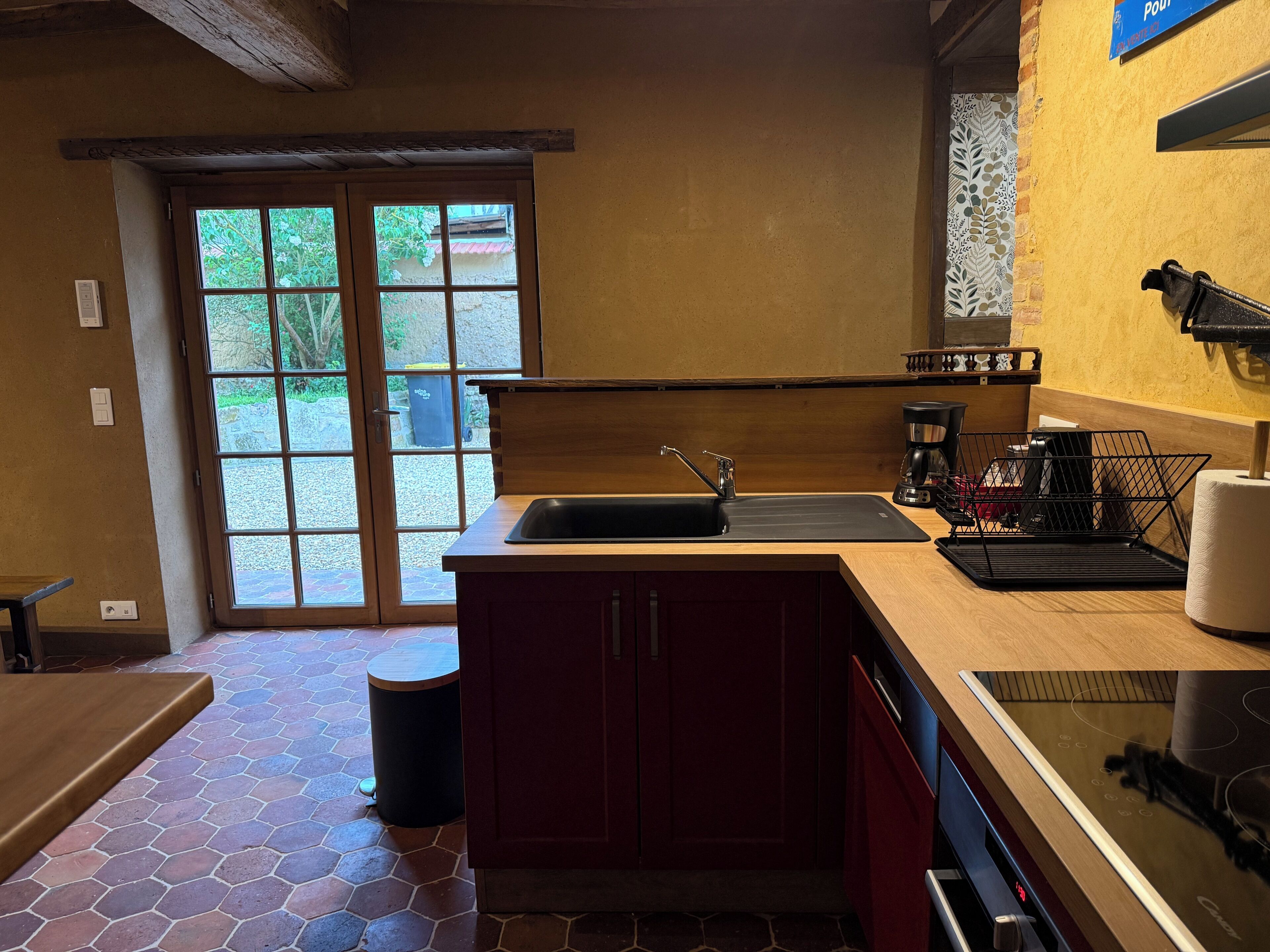 A kitchen with a wooden countertop, a sink, a coffee maker, and a window with a view of greenery.