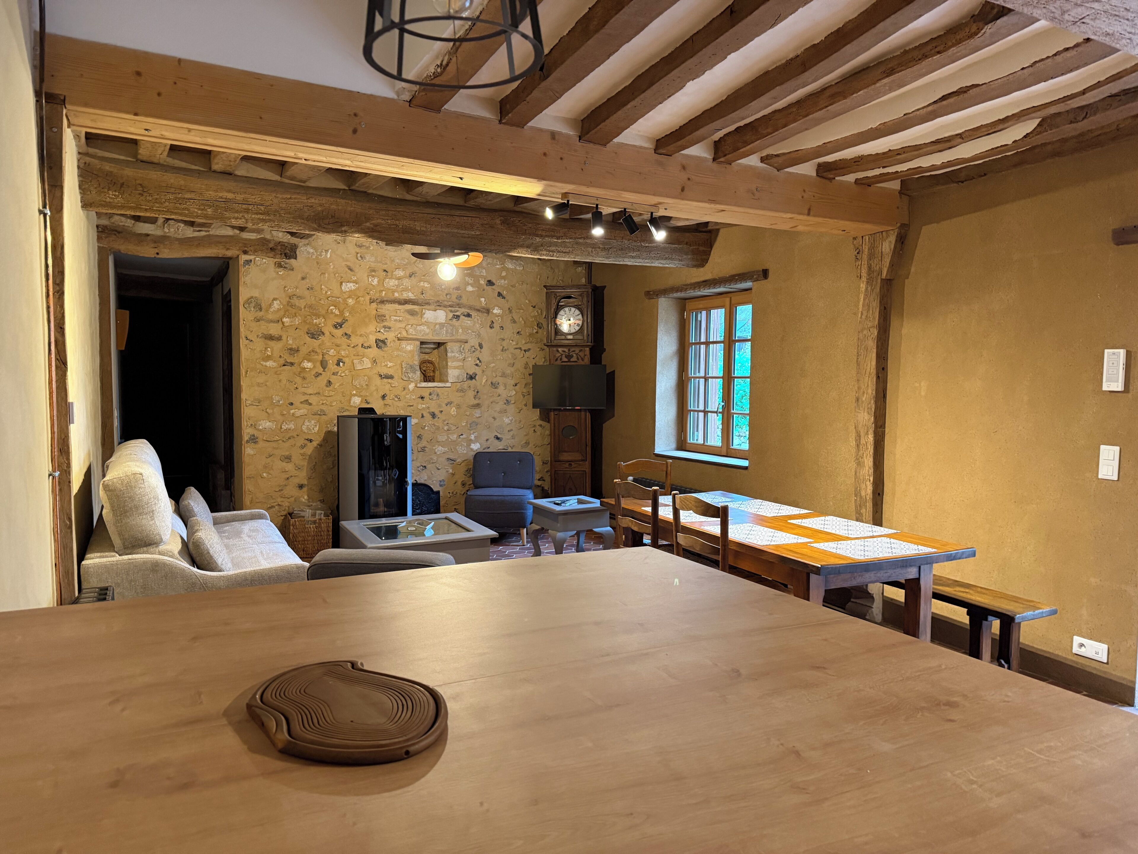 A rustic room with exposed beams, a stone wall, a wooden table, a sofa, a television, and a clock.