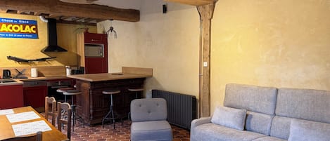 Un salón acogedor con techo de madera, una cocina con armarios rojos, un sofá gris y una mesa de comedor con sillas.