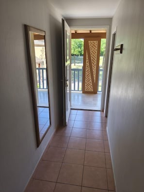 A hallway with a tiled floor leading to an open door with a decorative panel.