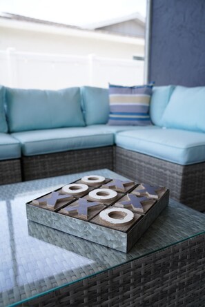 Ein Tisch mit Glasplatte und Geflochtkorb, ein blaues Sofa mit Kissen in Streifenmuster sowie ein Holzbrettspiel.