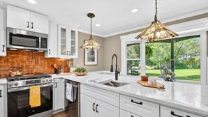 A modern kitchen with white cabinetry, stainless steel appliances, a large window, and a hanging light fixture. - Modern Farmhouse: 12.5 Acres & 2 Fire Pits (Lothian)