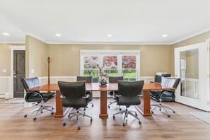 Une salle de confĂ©rence avec une table en bois, quatre chaises de bureau noires, une sculpture dĂ©corative reprĂ©sentant un cerf et une vue sur un jardin, visible Ă travers de grandes fenĂȘtres.