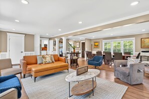 A spacious living area with a sofa, chairs, a dining table, and a kitchen in the background.