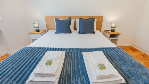 A neatly made bed with two pillows, two bedside tables with lamps, and a blue striped area rug. - Cedofeita Cozy by Hosty (Porto)