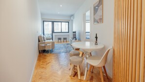 A modern living room with a sofa, a round dining table with chairs, a patterned rug, and a large window. - Cedofeita Cozy by Hosty (Porto)