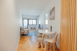 Ein modernes Wohnzimmer mit einer Couch, einem runden Esstisch mit Stühlen, einem gemusterten Teppich und einem großen Fenster.