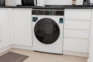 Eine kompakte, moderne Küche mit Einbauwaschmaschine, weißen Schränken und einer schwarzen Arbeitsplatte.