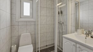 Un baño moderno con ducha de vidrio, inodoro, lavamanos y artículos de aseo, además de una ventana.