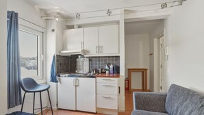 Cocina compacta con armarios blancos, una pequeña isla y un taburete de bar.