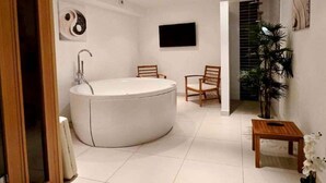 A modern bathroom with a freestanding bathtub, two wooden chairs, a small wooden table, and a potted plant. - MAGNIFICENT VILLA WITH POOL, SPA AND SEA VIEW (Cerbère)