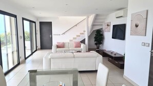 A modern living room with a white sofa, a glass coffee table with fruit, and a staircase leading to an upper level. - MAGNIFICENT VILLA WITH POOL, SPA AND SEA VIEW (Cerbère)
