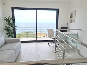 Een modern appartement met balkon, een bank, bureau en een potplant.