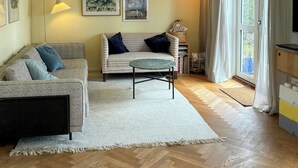 A living room with a sofa, a small round table, a floor lamp, and a large window with curtains. - Townhouse with art and terrace (København)