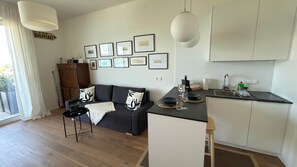 A modern living room with a sofa, a coffee table, and a kitchen area with a sink and countertop. - Hermitage Apartment E03B - Lake View & Access (Maria Wörth)