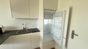 A kitchen with a sink, cabinets, and an open refrigerator. - Hermitage Apartment E03B - Lake View & Access (Maria Wörth)
