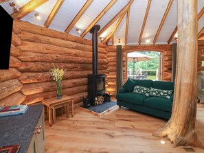A log cabin interior with a fireplace, a sofa, a dining area, and a view of the outdoors.