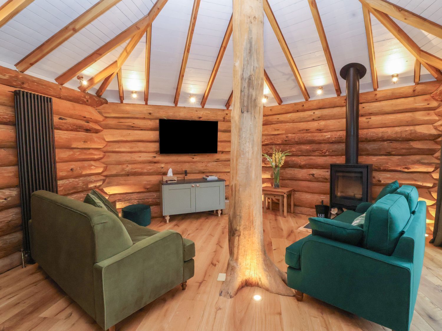 Ein rustikales Blockhaus-Interieur mit Fernseher, Sofa, Kamin und Holzbalkendecke.