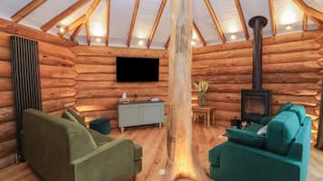 Ein rustikales Blockhaus-Interieur mit Fernseher, Sofa, Kamin und Holzbalkendecke.