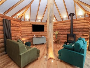 A log cabin interior with a wooden ceiling, a fireplace, a flat-screen TV, and green sofas. - Copper Suite (Chulmleigh)