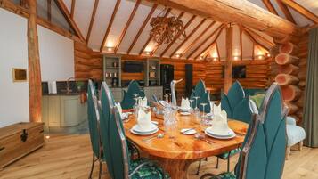 A log cabin interior with a dining table set for four, surrounded by green upholstered chairs.