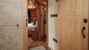 A wooden door with a carved leaf design, a bed with a green pillow, and a wooden ceiling structure.