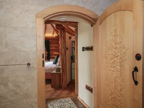 A wooden door with a carved leaf design, a bed with a green pillow, and a wooden ceiling structure. - Copper Suite (Chulmleigh)