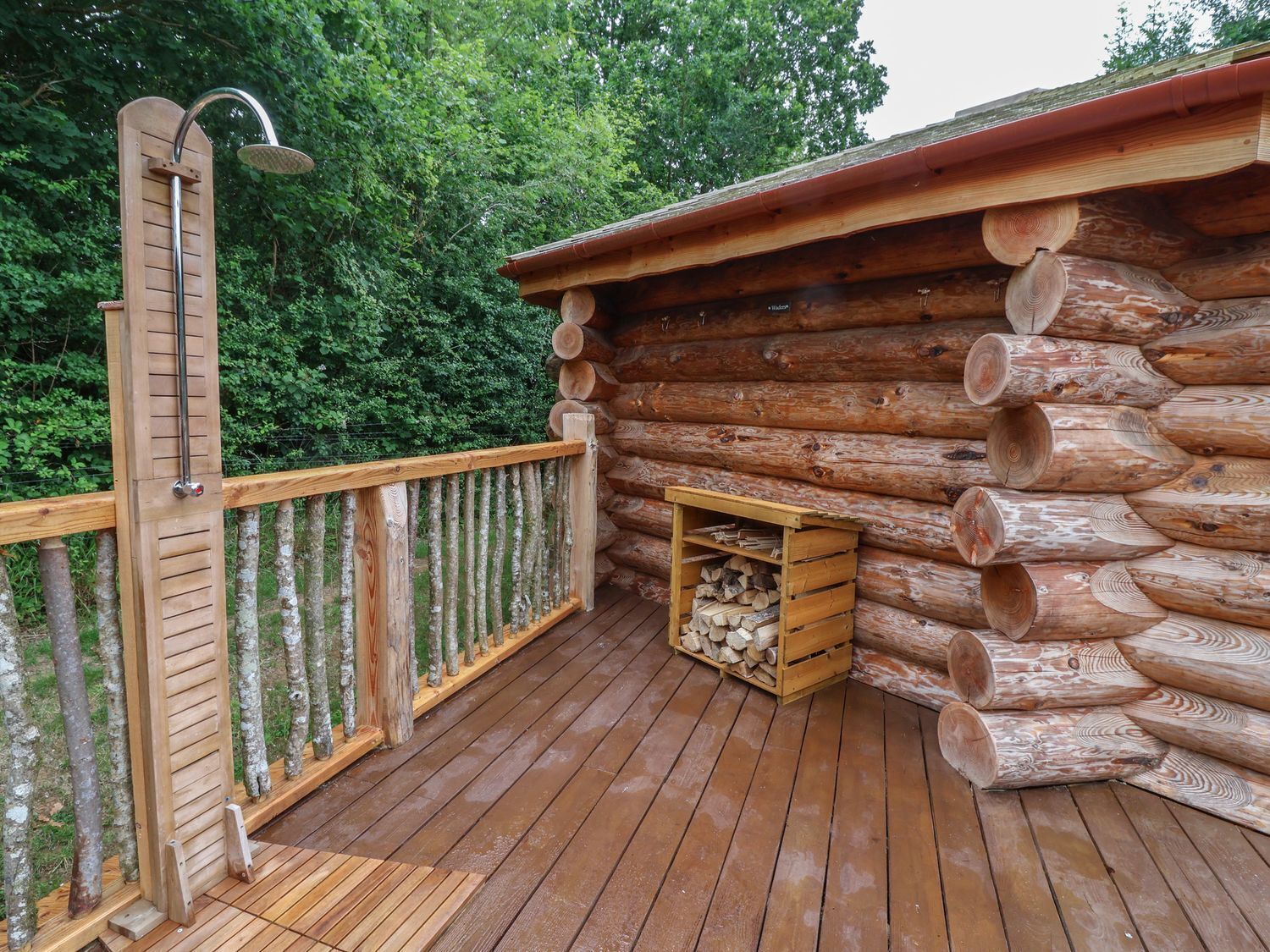 A wooden deck with a metal railing, a wooden bench, and a log cabin structure with a firewood storage area.