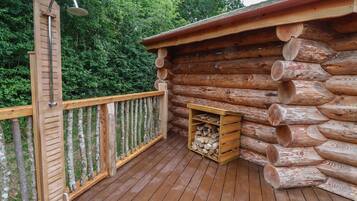 A wooden deck with a metal railing, a wooden bench, and a log cabin structure with a firewood storage area.