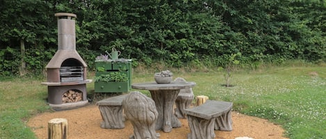 An outdoor patio with a stone fireplace, a green planter, and a round table surrounded by stools.