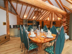 A log cabin interior with a dining table set for four, surrounded by green upholstered chairs. - Copper Suite (Chulmleigh)
