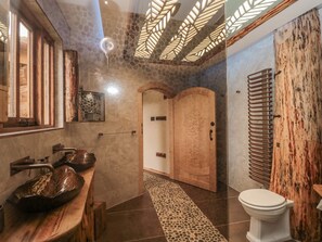 A modern bathroom with a wooden vanity, a large sink, a shower with a wooden door, and a glass-enclosed toilet. - Copper Suite (Chulmleigh)
