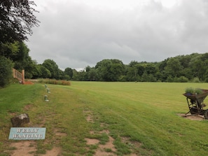 A grassy field with a wooden staircase, a wheelbarrow with plants, and a sign reading 'WELLY WANGING'. - Copper Suite (Chulmleigh)