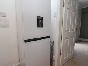 Uma porta branca com etiqueta de dispensador de água, uma parede branca com etiqueta de lixeira para reciclagem e uma porta com puxador.