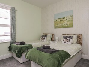 Ein Schlafzimmer mit zwei Betten, einem Fenster mit Vorhängen, einem Bild an der Wand und einem Nachttisch mit einer Lampe.