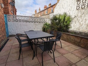 Eine Terrasse mit Tisch und Stühlen, ein weißes Ziergitter und eine Backsteinmauer.
