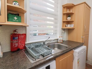 Eine Küche mit einer Granit-Arbeitsplatte, einer Edelstahl-Spüle, einem Geschirrspüler und einem Fenster mit Jalousien.