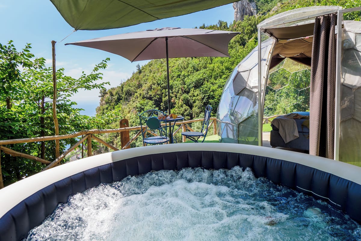 Ein Whirlpool im Freien mit Blick auf eine Berglandschaft, eine Holzterrasse und ein Tisch mit Stühlen.